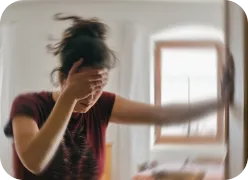 A person standing with eyes closed, holding a wall or railing to steady themselves.